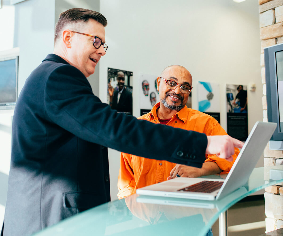 Two men standing near laptop on table
